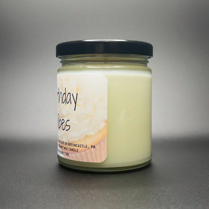 Angled view of the Birthday Vibes candle by Elysium Candle Co., with a soft-focus label featuring a swirl reminiscent of birthday cake, hand-poured in small batches.