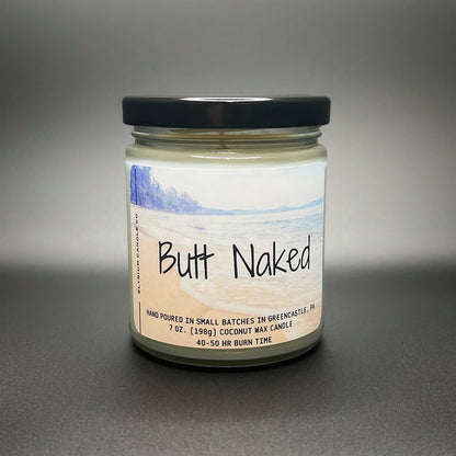 A playful ‘Butt Naked’ coconut soy wax candle by Elysium Candle Co., featuring a serene beach scene on the label, with a promise of 40-50 hours of burn time.