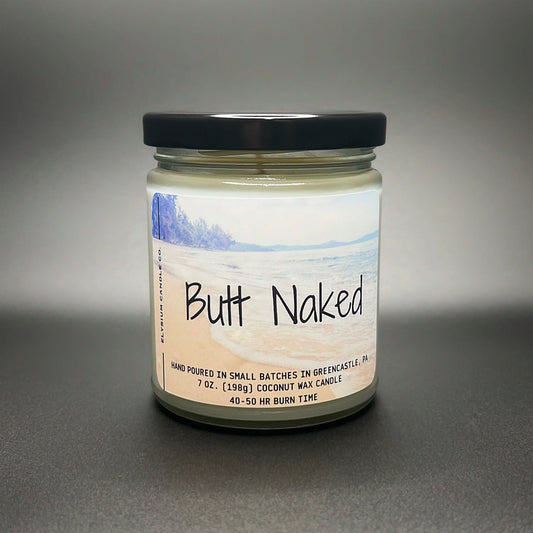 A playful ‘Butt Naked’ coconut soy wax candle by Elysium Candle Co., featuring a serene beach scene on the label, with a promise of 40-50 hours of burn time.