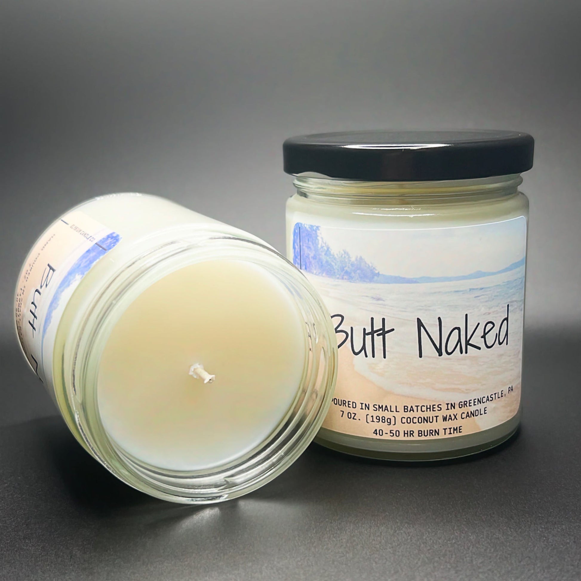 An open jar view of the Butt Naked candle from Elysium Candle Co., highlighting the pure coconut soy wax and a beach-themed label that evokes a sense of calm.