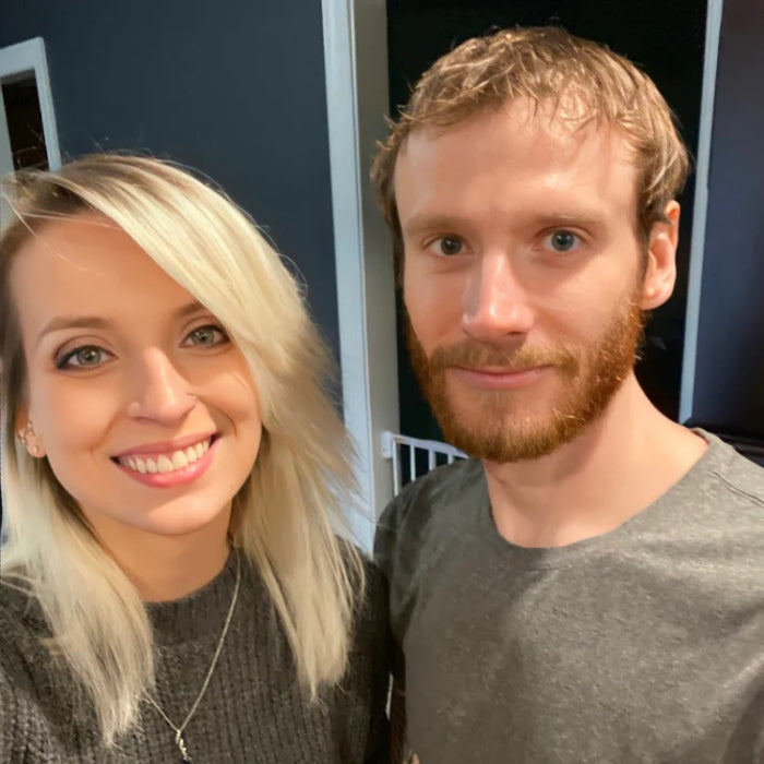 A smiling couple, the proud owners of the candle business, stand together exuding warmth and friendliness, with a homey ambiance in the background, representing the personal touch behind their handcrafted products.