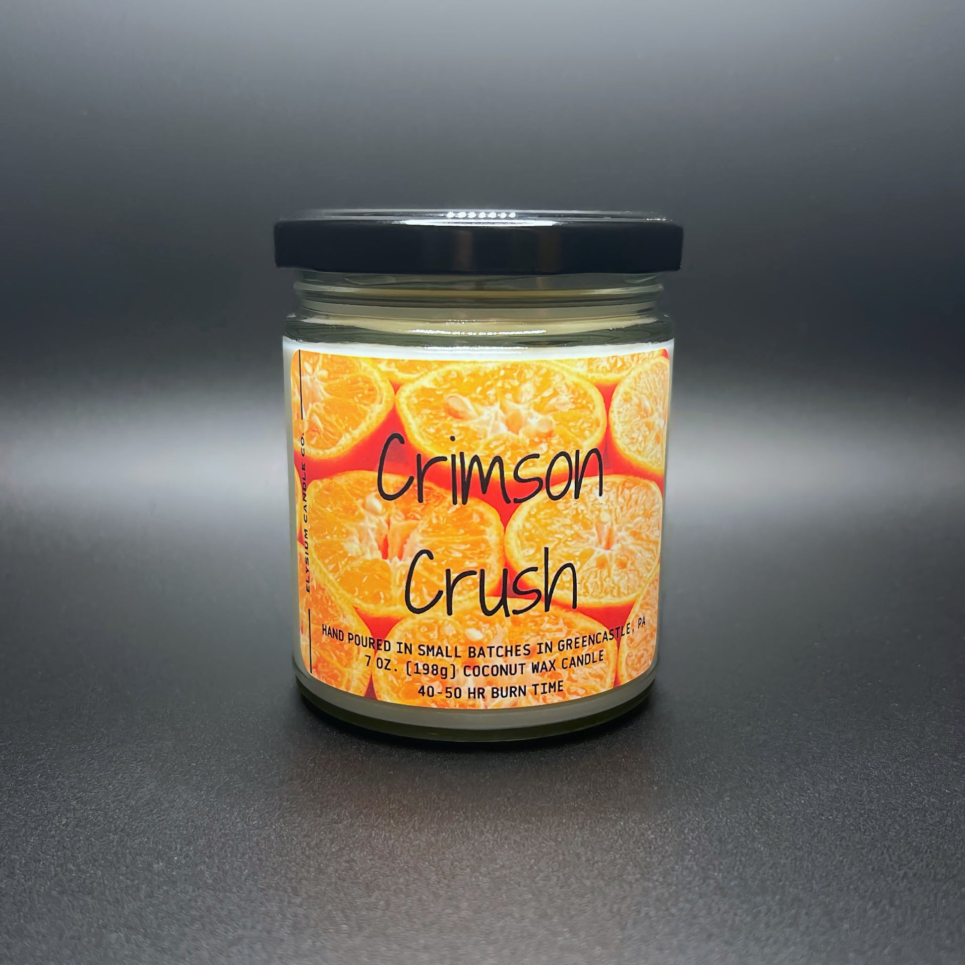 Front view of unlit Crimson Crush candle, citrus label, in soft lighting.