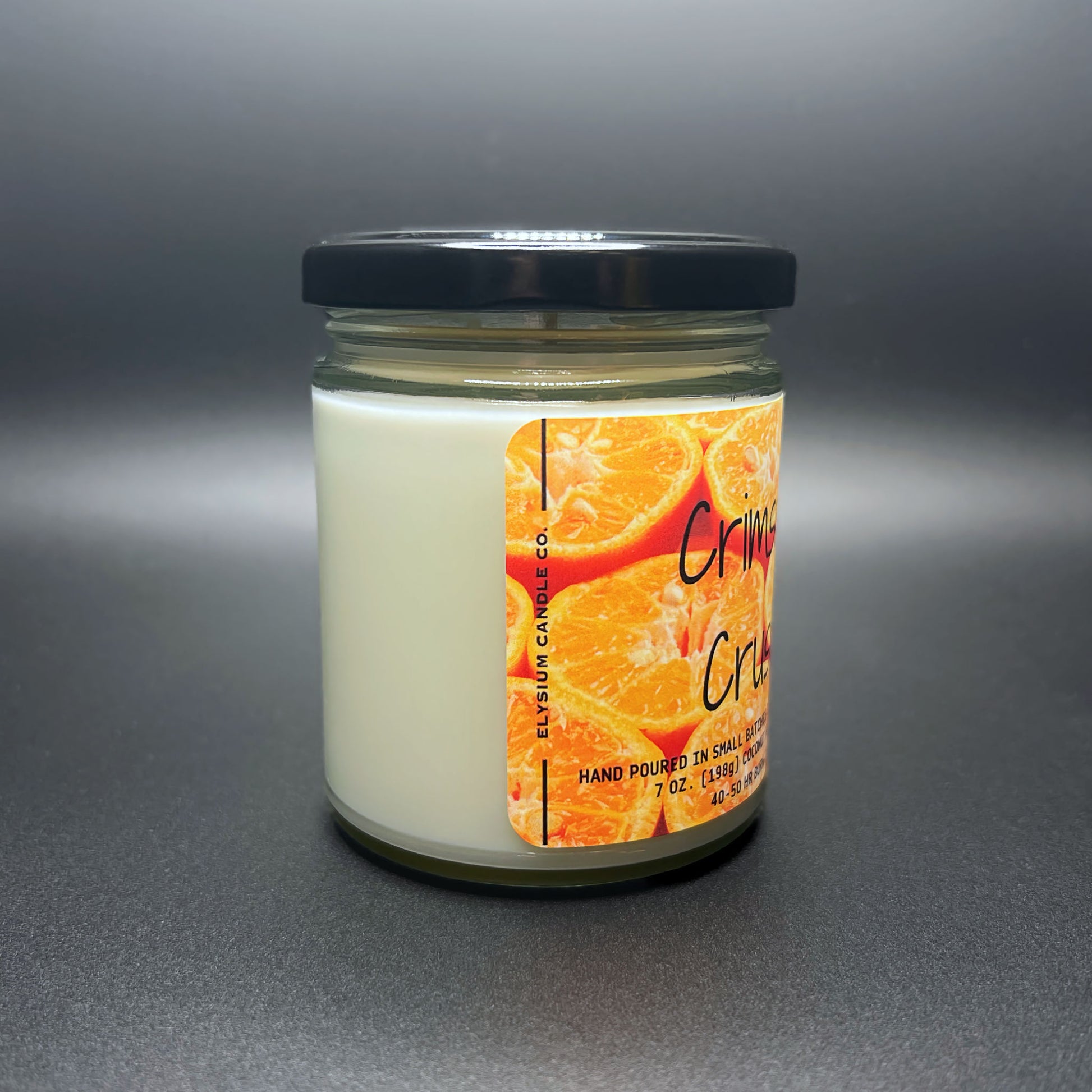 Crimson Crush candle, creamy white, black lid, vibrant orange label, grey backdrop.