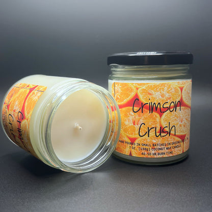 Open Crimson Crush candle, white wax, bright citrus label, grey surface.