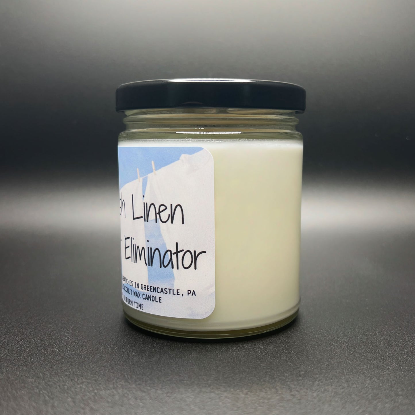 Angled view of the ‘Fresh Linen Odor Eliminator’ coconut soy candle, highlighting the eco-friendly wax, the sturdy jar, and the detailed label with burn time information.