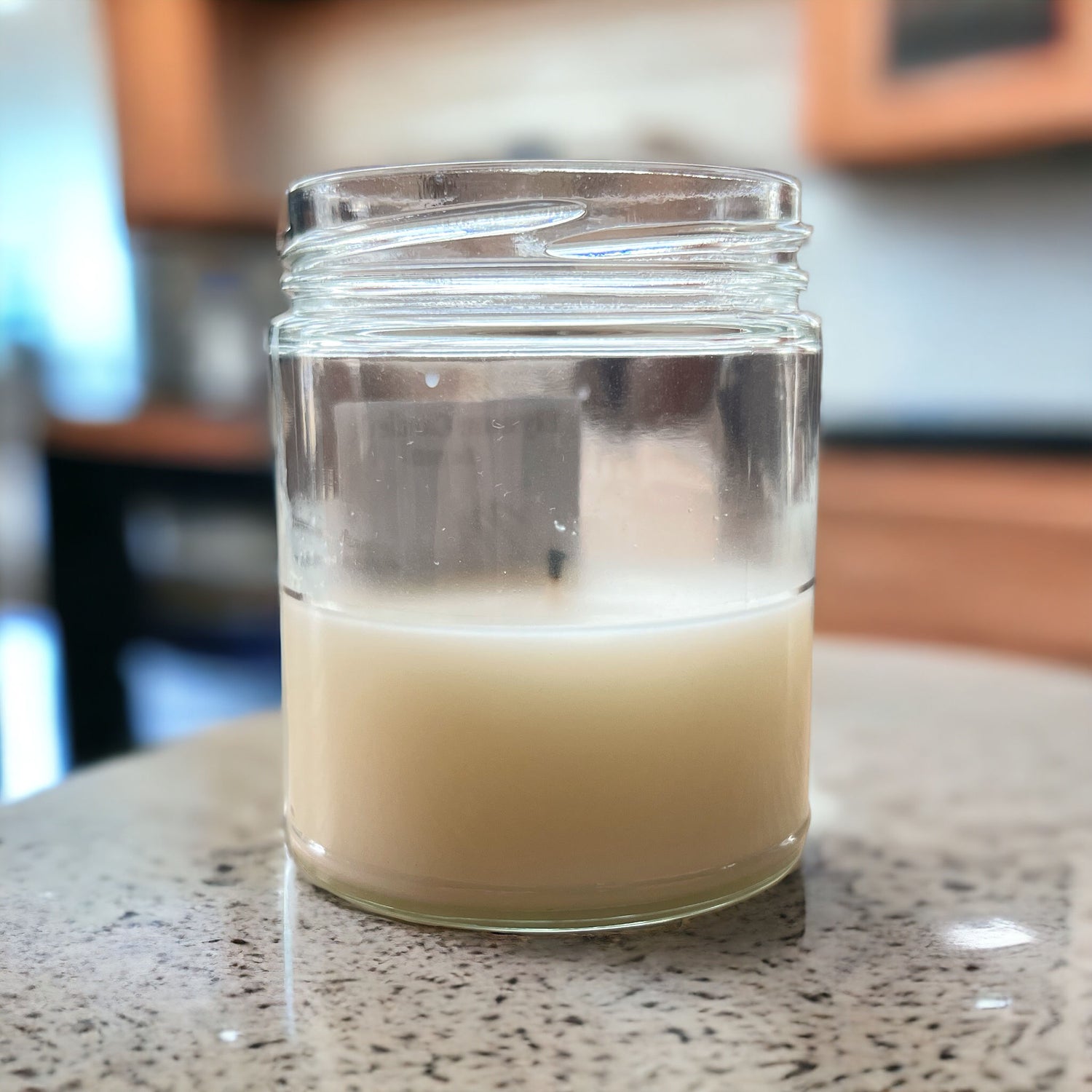 A hand-poured coconut soy blend candle in a clear glass jar, set on a kitchen countertop, symbolizing a non-toxic and vegan candle product.