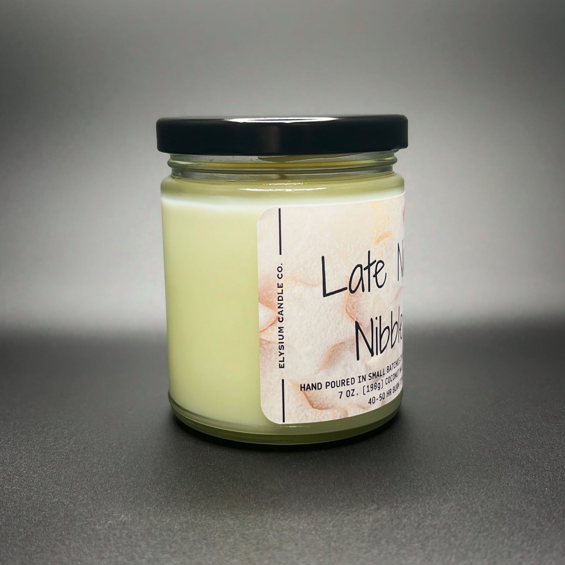 Side view of a 7 oz Late Night Nibbles candle by Elysium Candle Co., displaying the creamy coconut soy wax blend and a playful watercolor snack design label.