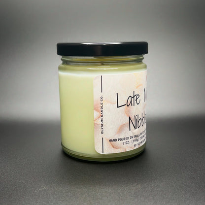 Side view of a 7 oz Late Night Nibbles candle by Elysium Candle Co., displaying the creamy coconut soy wax blend and a playful watercolor snack design label.