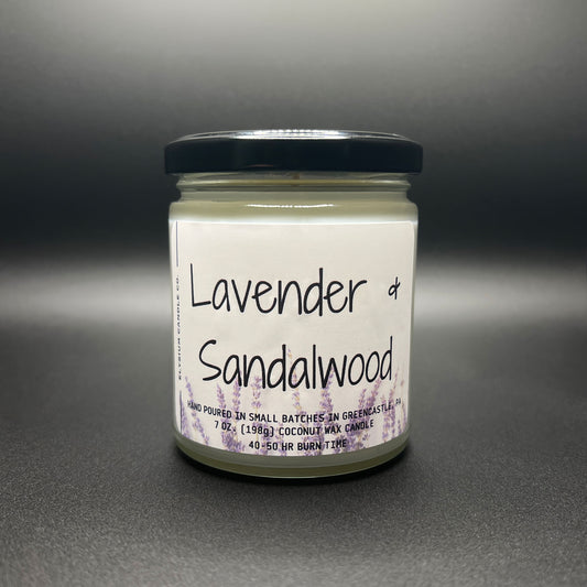 Frontal view of Elysium Candle Co.’s Lavender and Sandalwood coconut-soy candle, clearly showing the white label with elegant lavender sprig designs and the scent name. The candle, encased in a glass jar with a black lid, communicates handcrafted quality.
