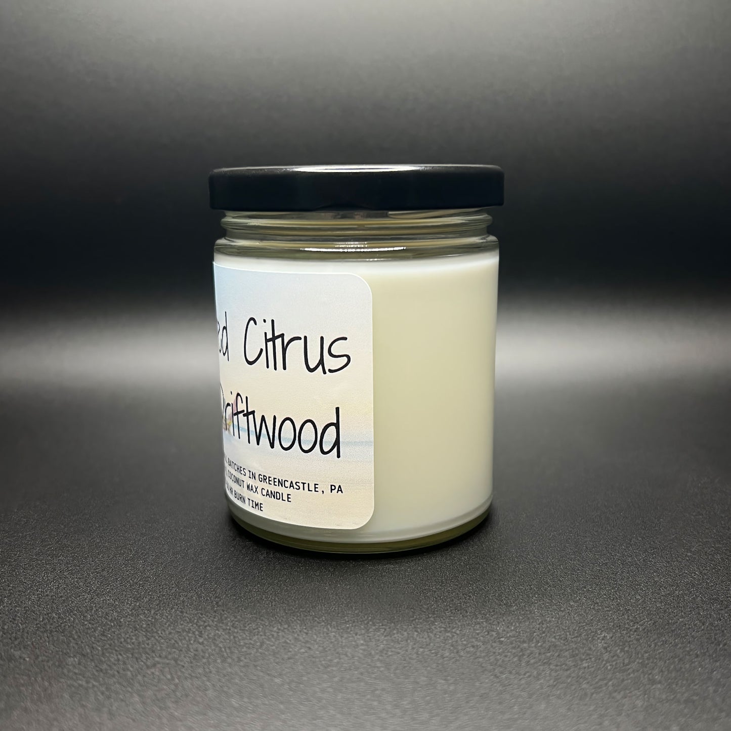 Angled view of the Salted Citrus and Driftwood coconut wax candle, with emphasis on the label that bears the Elysium Candle Co. branding and the beach-inspired artwork, indicating its handcrafted nature and burn time.